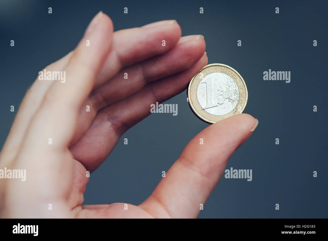 Business woman holding one euro coin between fingers, close up with selective focus Stock Photo