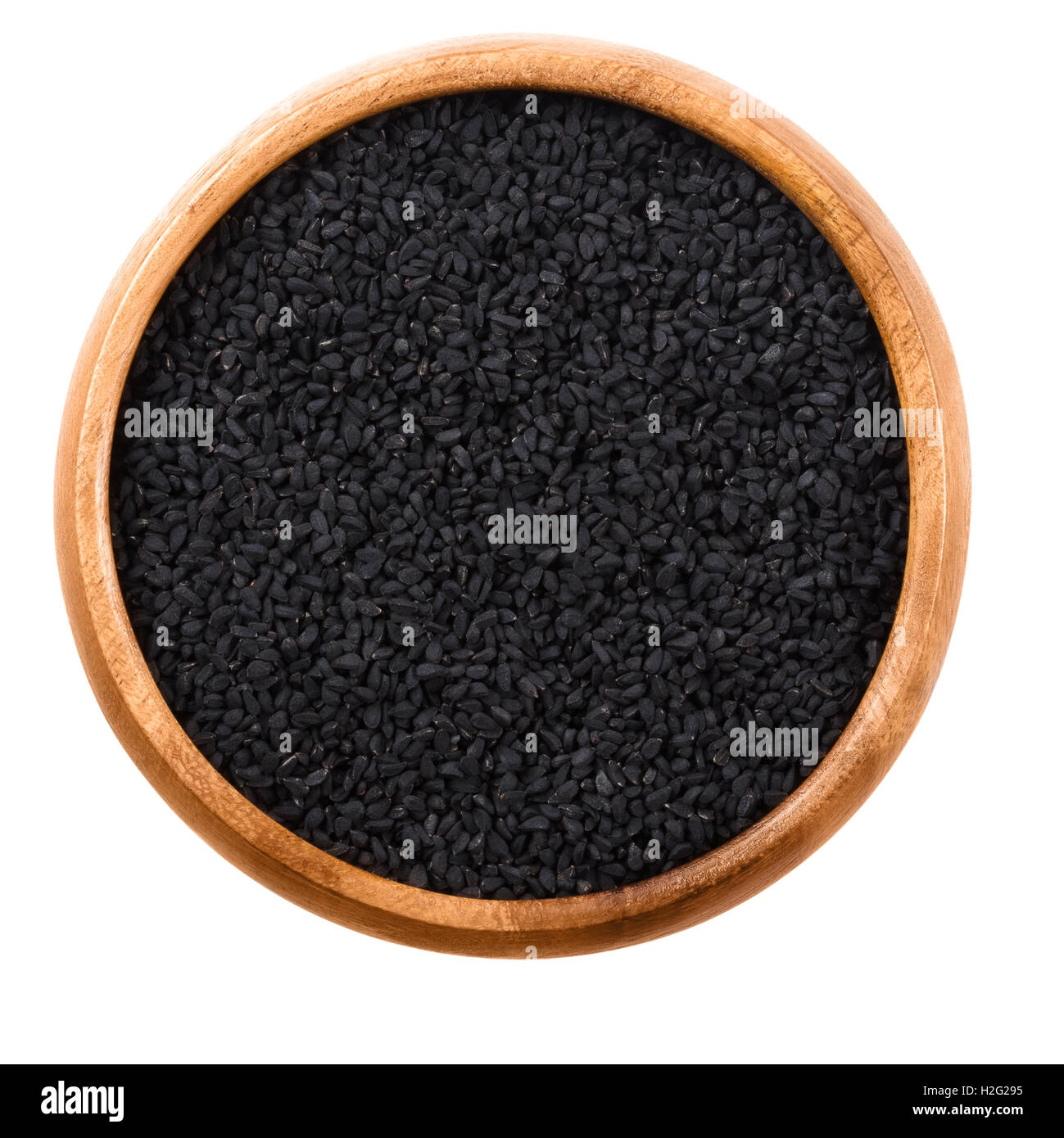 Black cumin seeds in wooden bowl over white. Dried whole fruits of Nigella sativa, also black caraway, nigella or kalonji. Stock Photo