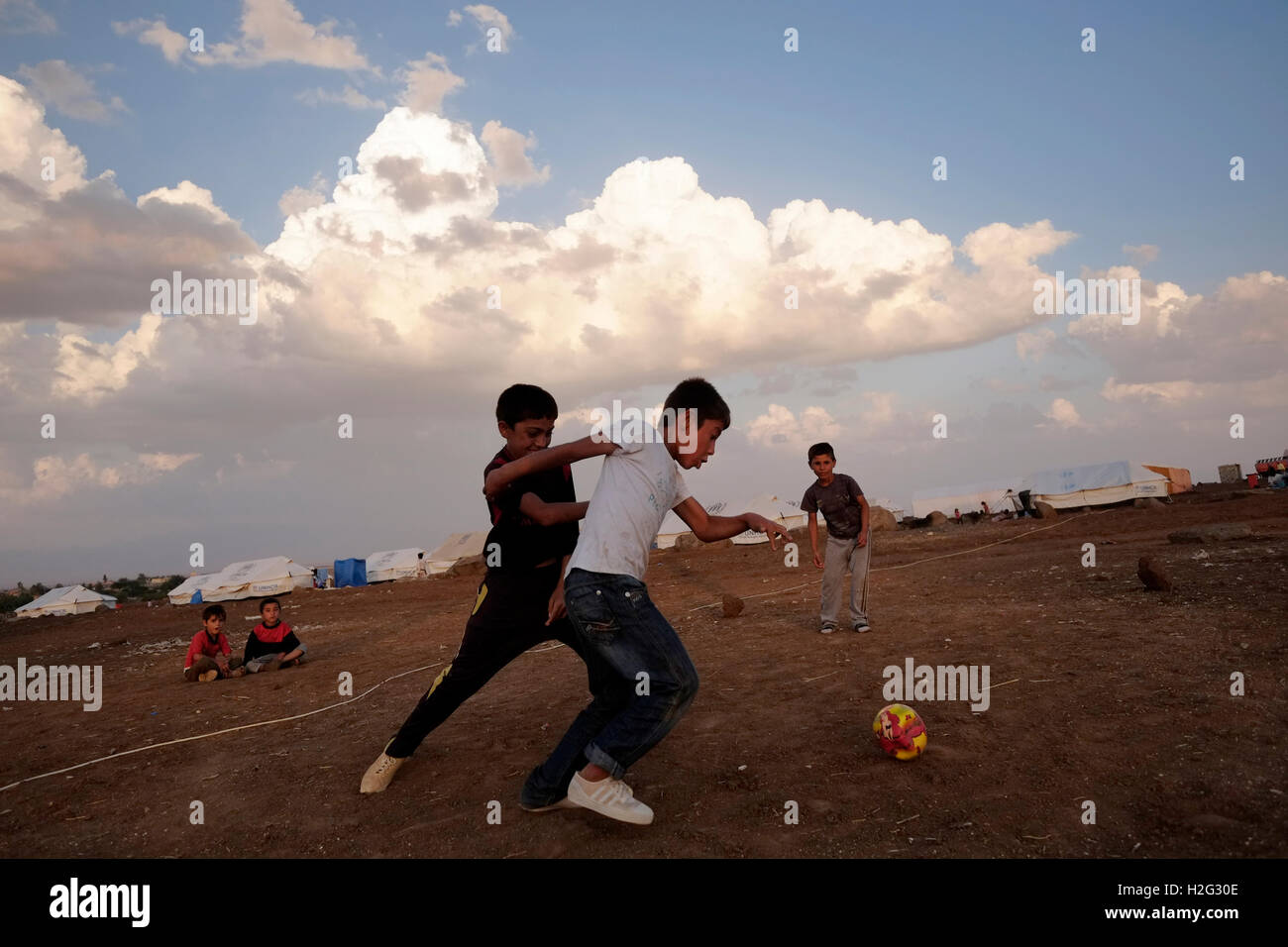 Yazidi children playing football in Nawroz refugee camp which was initially established to shelter Syrians displaced from the ongoing Syrian civil war then occupied by displaced people from the minority Yazidi sect, fleeing the violence in the Iraqi town of Sinjar situated next to the town of al-Malikyah in Rojava autonomous Kurdish region, North Eastern Syria. Stock Photo