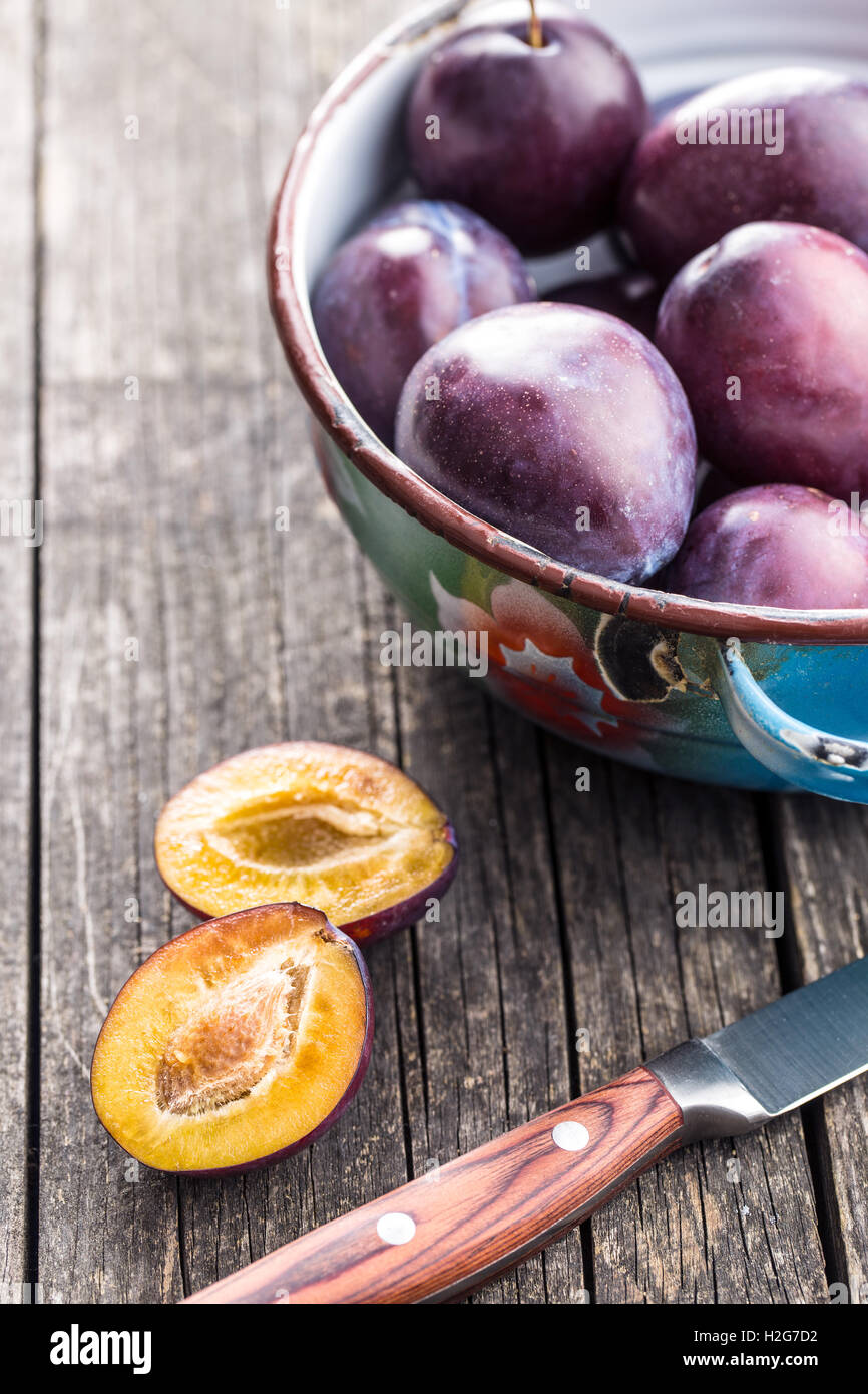 Halved ripe plums and knife on old wooden table. Stock Photo