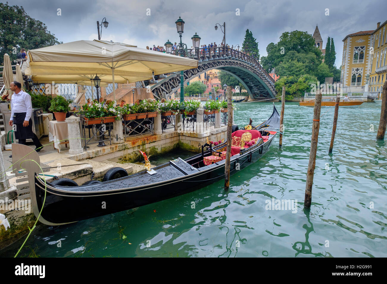 Venice. Restaurant with moored gondola near Accademia Bridge on Grand  Canal. Tourists pizzeria. Mooring poles in water Stock Photo - Alamy