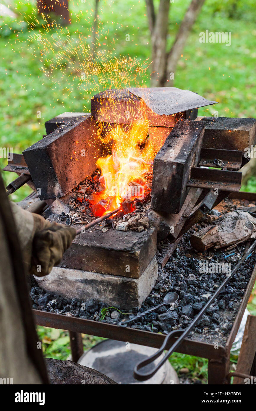 Blacksmith heats iron rod in rural forging furnace with burning coals Stock Photo