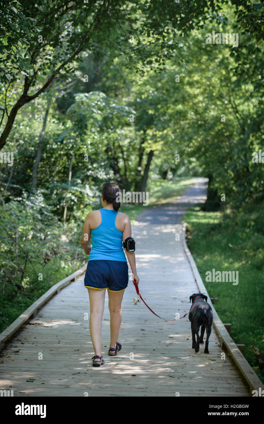 Woman, wearing fitness tracker, and dog walking on a trail Stock Photo