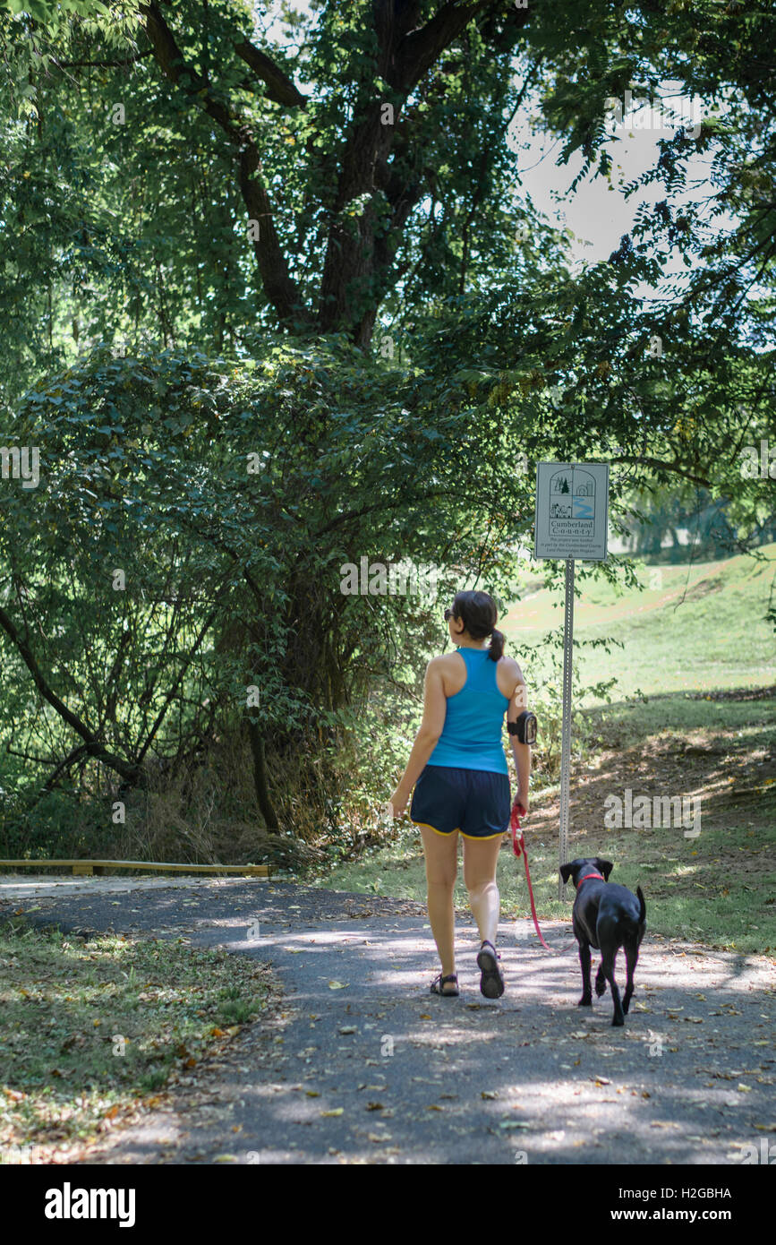 A woman, wearing fitness tracker, and her dog walking on a public trail Stock Photo