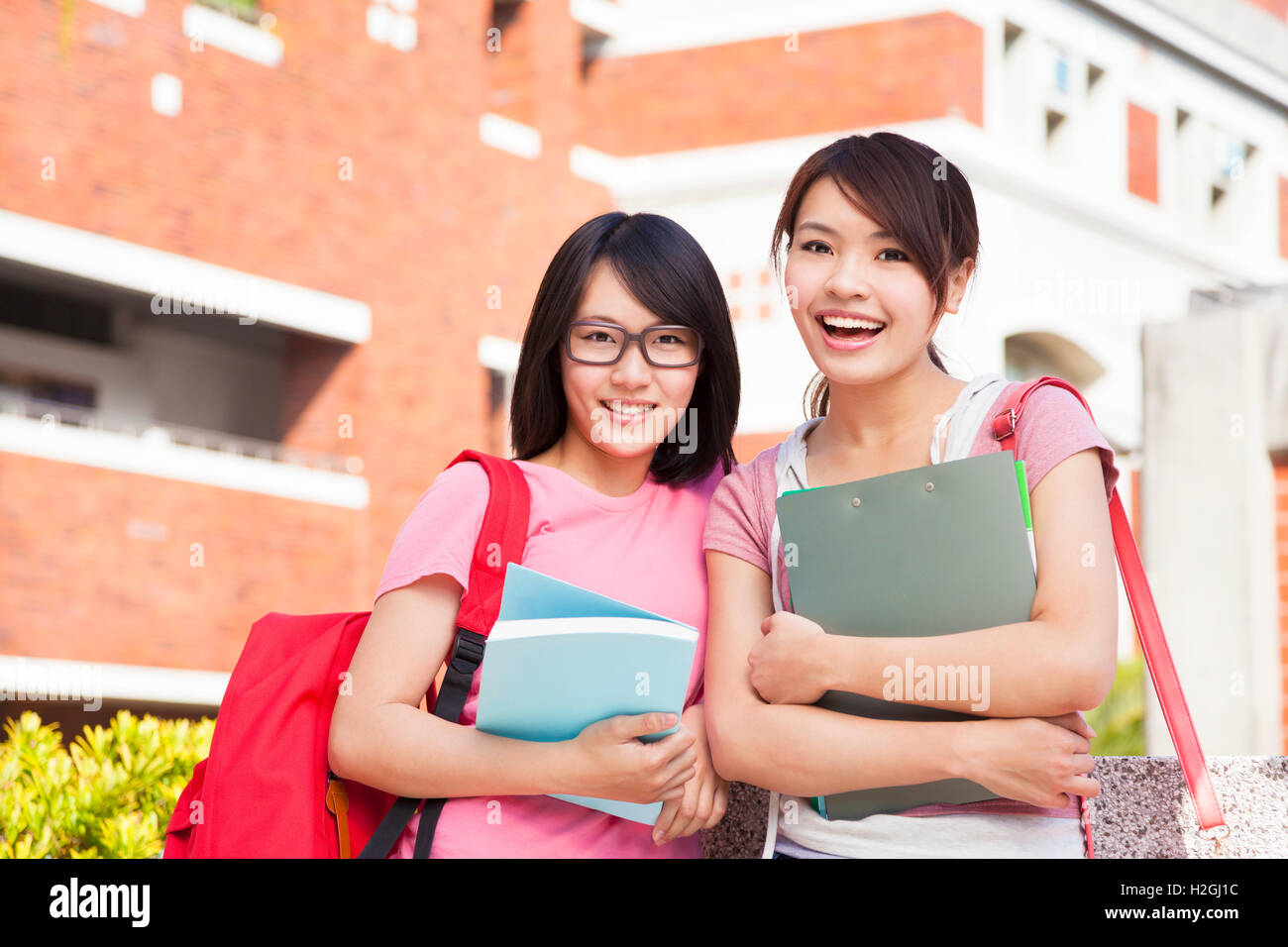 two smiling students holding books at campus Stock Photo - Alamy