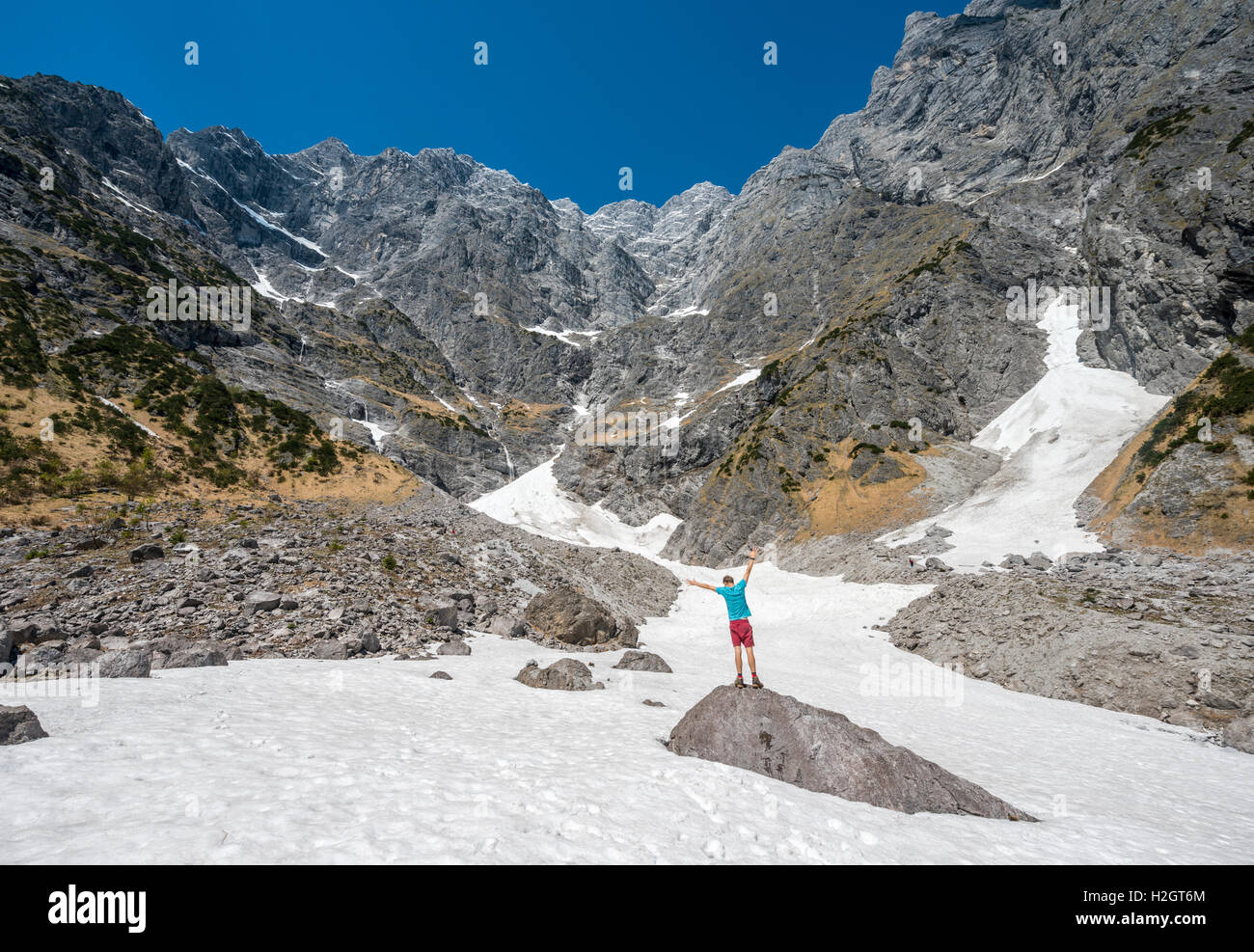 Young man on rock, snow field, Watzmann eastern slope, Berchtesgaden District, Upper Bavaria, Bavaria, Germany Stock Photo