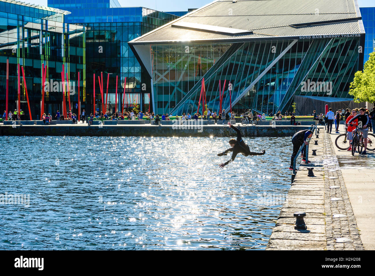 Boys jump into water at Hanover Quay on Dublin’s Grand Canal with Bord Gáis Energy Theatre behind Stock Photo