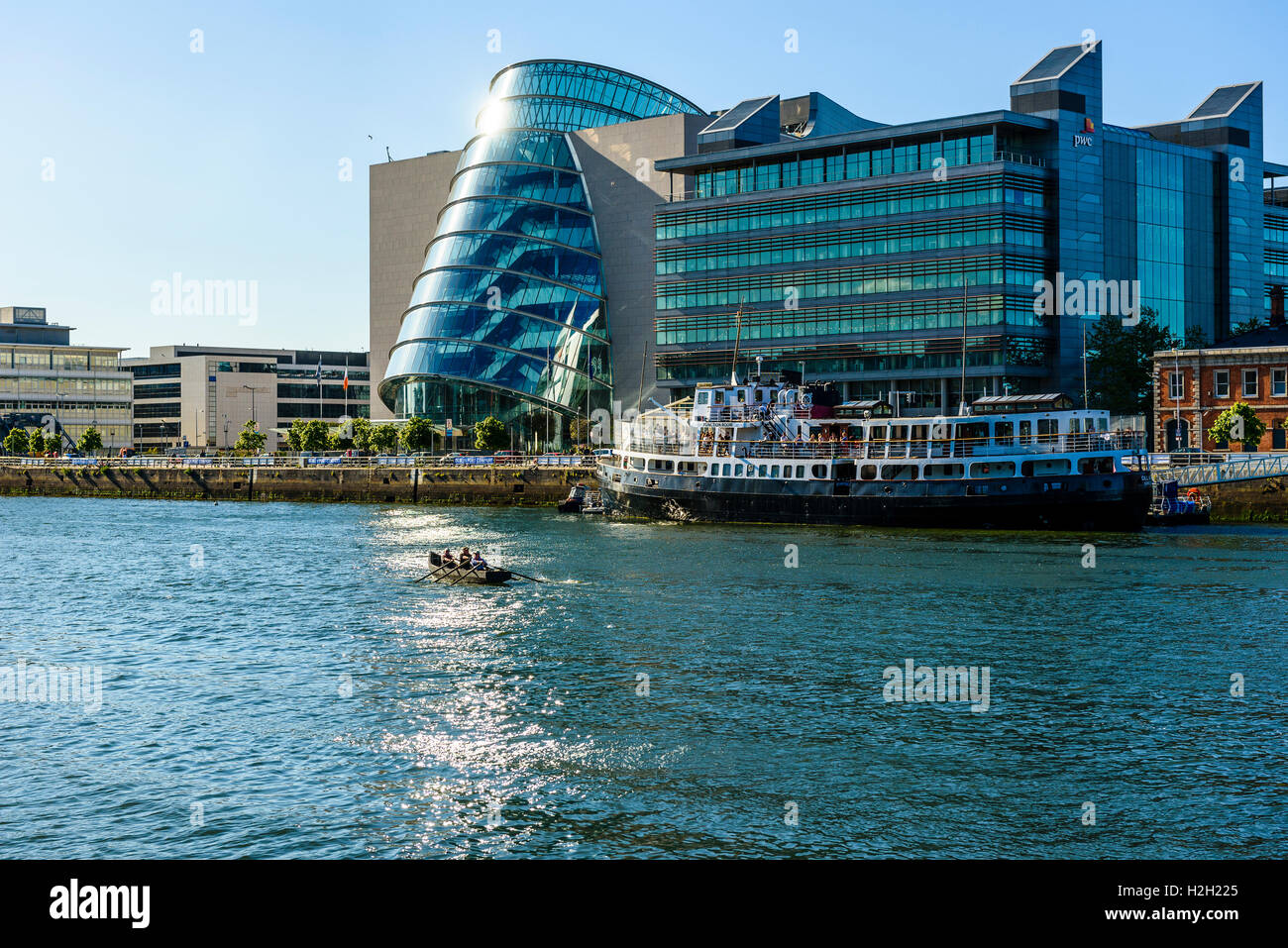 Dragon boat on River Liffey Dublin Ireland with Convention Centre Dublin, offices of pwc, and MV Cill Airne floating Restaurant Stock Photo