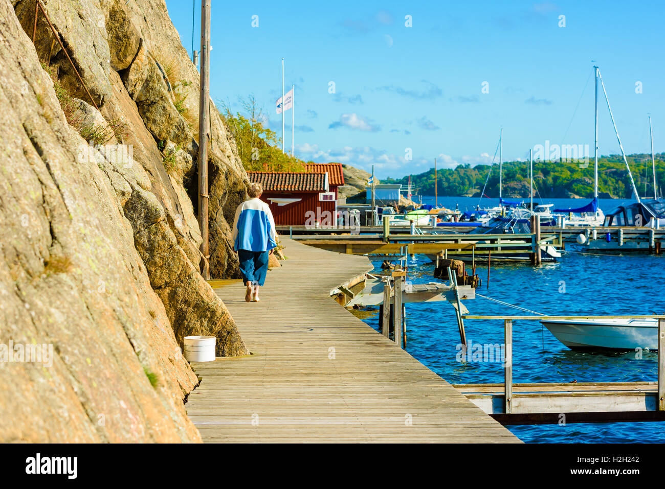Nosund, Sweden - September 9, 2016: Real life documentary of senior female taking a walk along the seaside pier with steep cliff Stock Photo