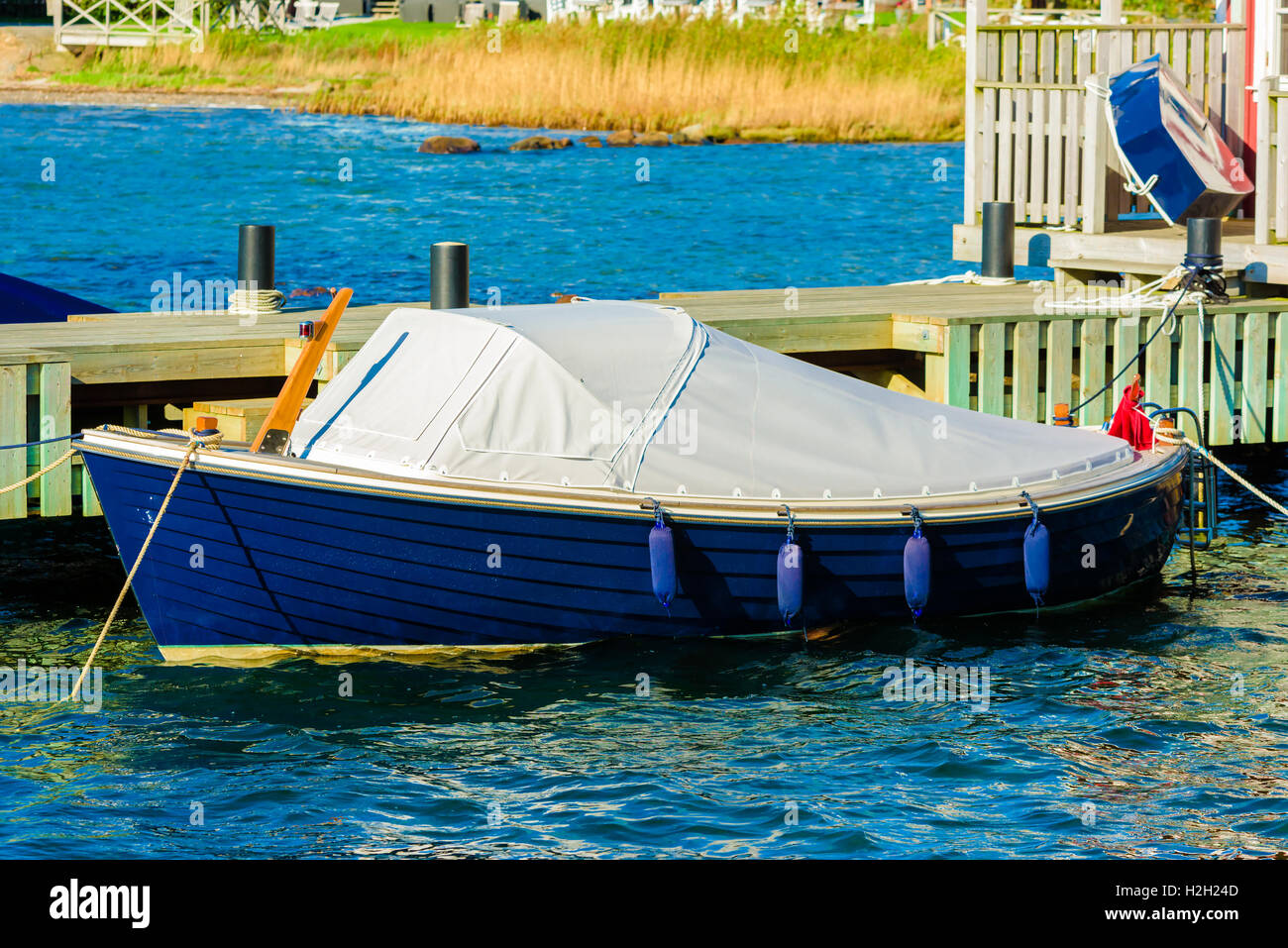 Blue motorboat covered with tarp, moored by a wooden pier. Stock Photo