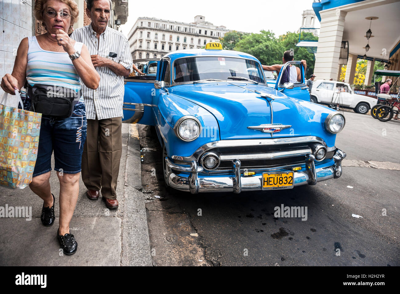 HAVANA - JUNE 12, 2011: Cubans pass a classic American car share taxi waiting for customers with open doors on the street. Stock Photo