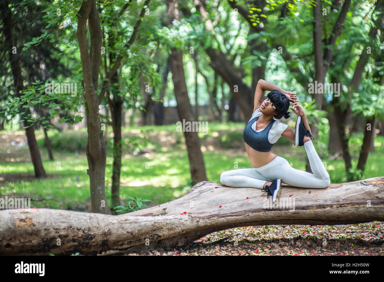 Young woman doing yoga poses on a tree trunk in a park in India Stock ...