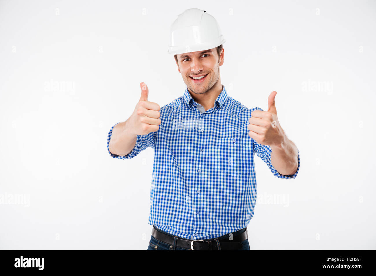Cheerful young man engeneer in building helmet showing thumbs up with both hands over white background Stock Photo