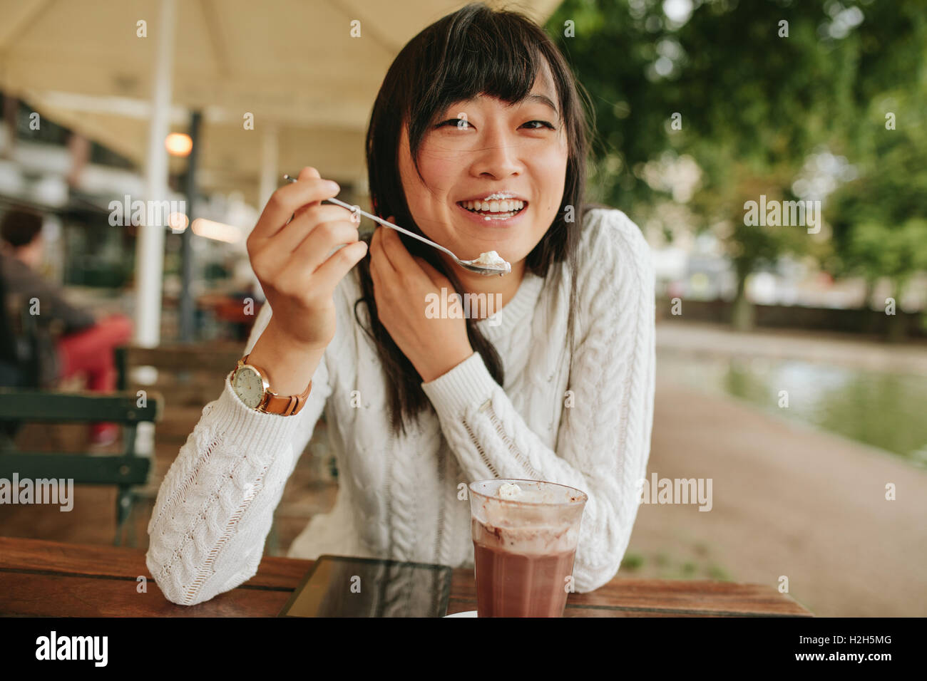 Shot of happy young woman at outdoor cafe eating cold dessert of ice cream. Chinese female enjoying dessert at coffee shop. Stock Photo