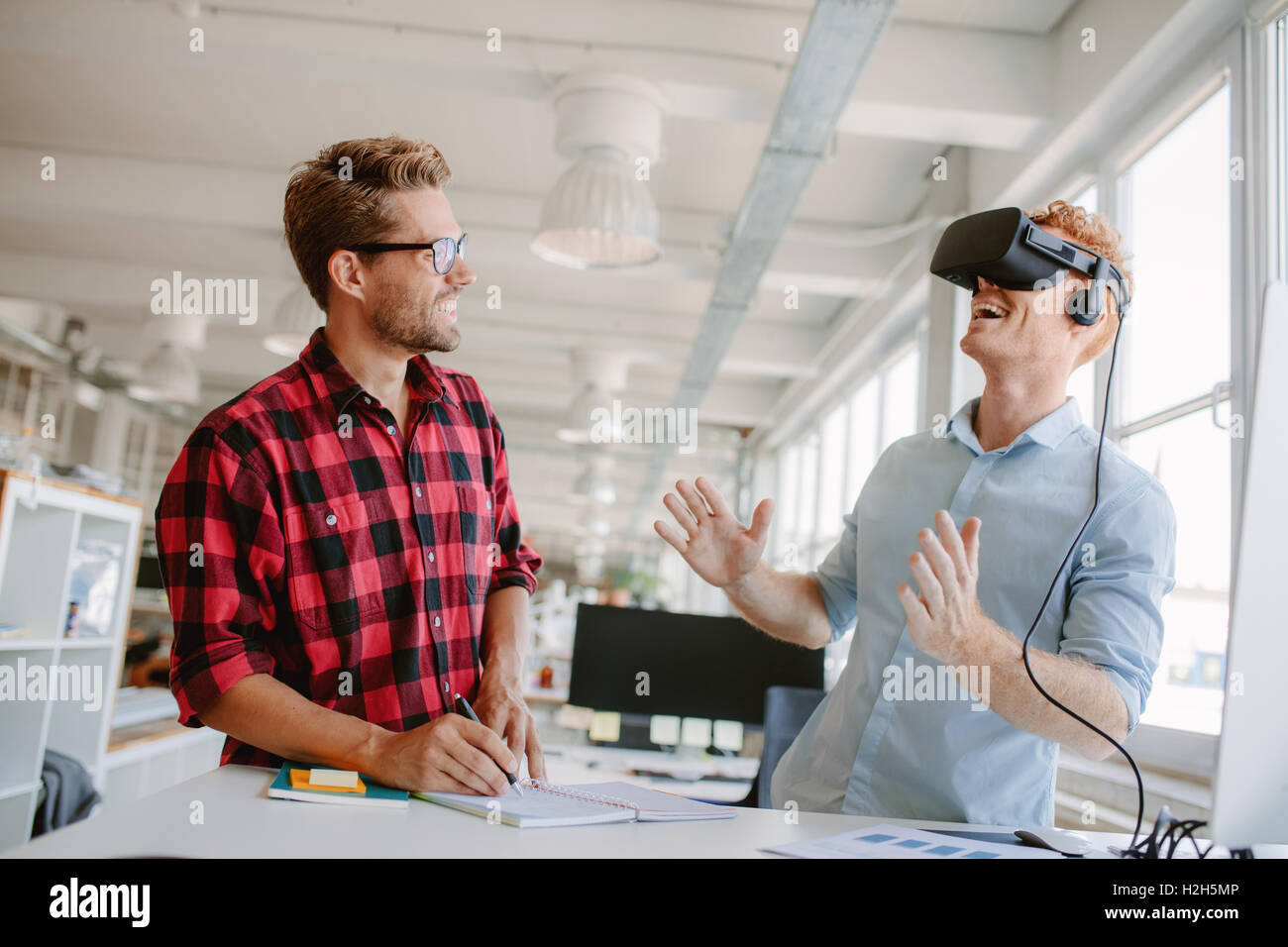 Young man testing virtual reality technology with colleague in office. Colleagues working on improving VR headset technology exp Stock Photo