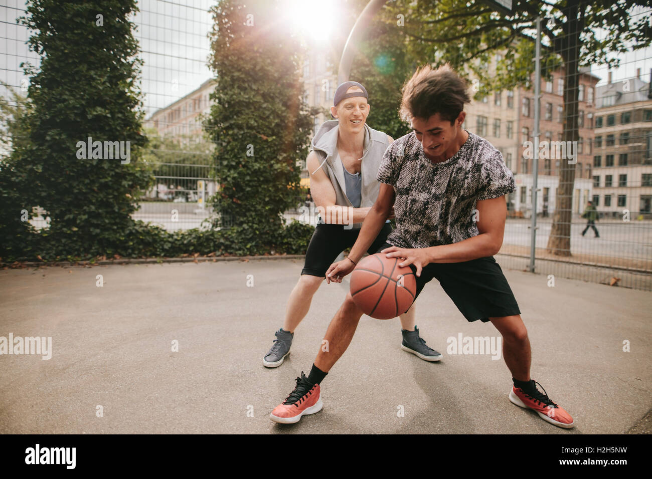 Two young man on basketball court dribbling with ball. Friends playing basketball on court and having fun. Stock Photo
