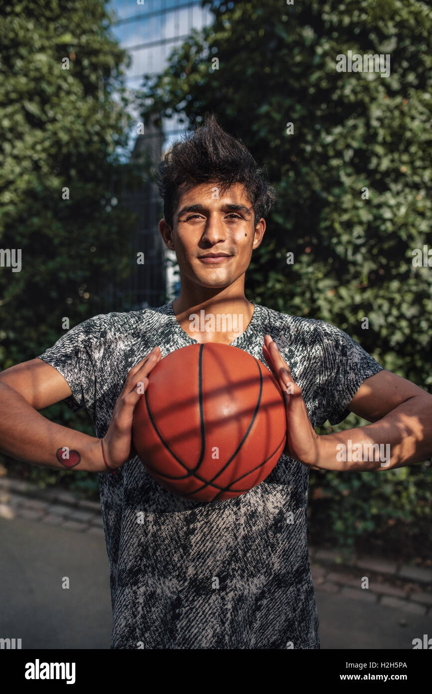 Portrait of young basketball player holding a ball. Teenage streetball player on outdoor court looking at camera with ball in ha Stock Photo