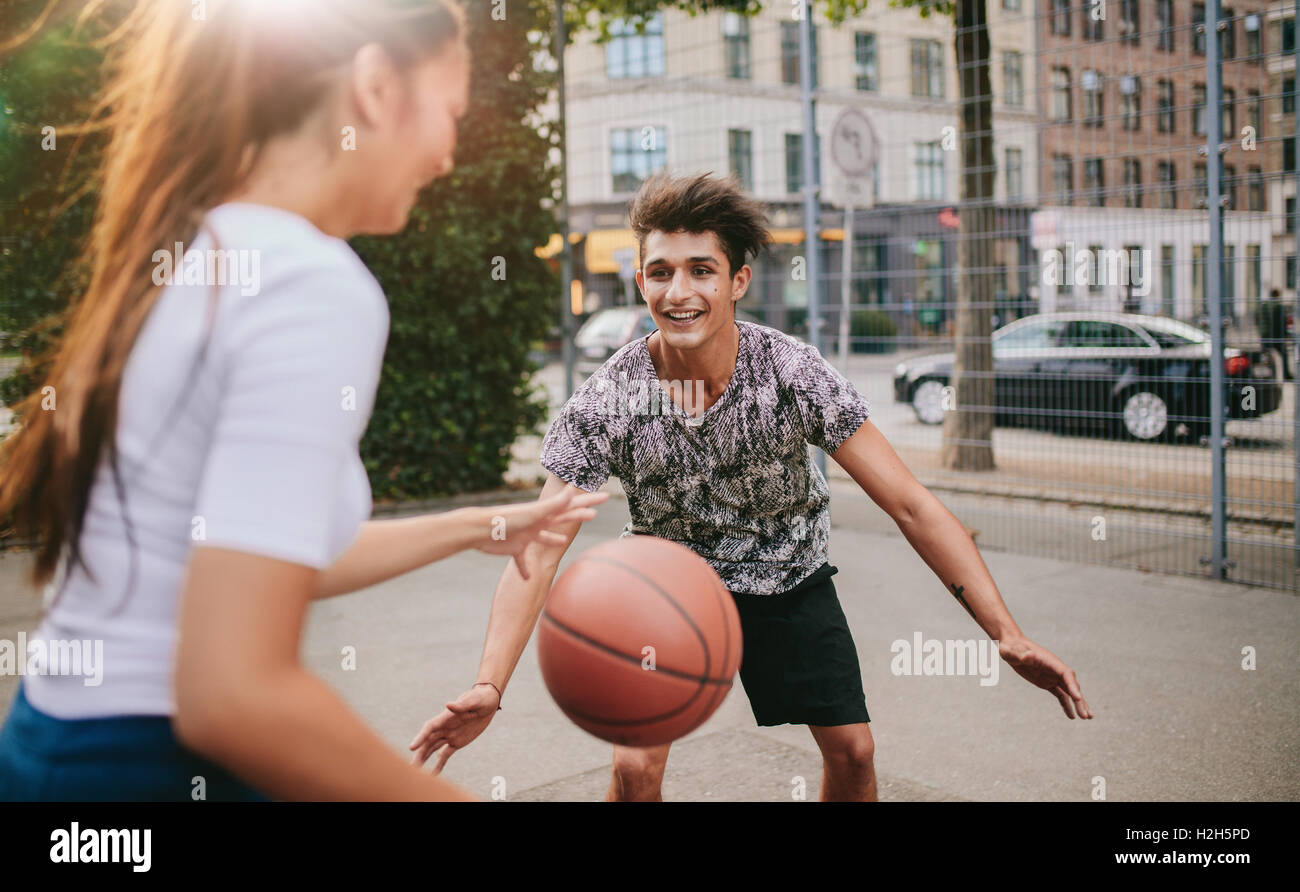 Two young man and woman playing  basketball on outdoor court. Friends having a game of basketball. Stock Photo