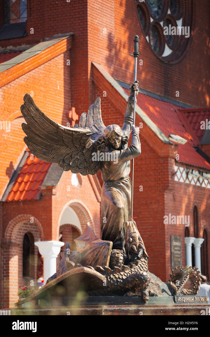 Statue Of Archangel Michael With Outstretched Wings, Thrusting Spear Into Dragon near Red Catholic Church Of St. Simon And St. H Stock Photo