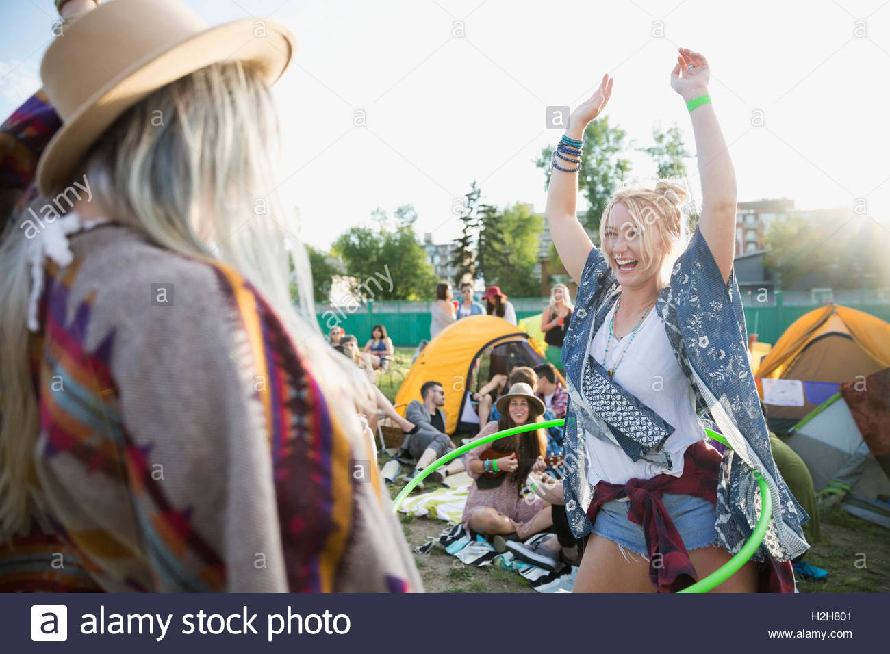 Playful young woman spinning with plastic hoop at summer music festival campsite Stock Photo