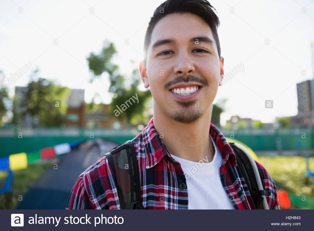 Portrait smiling young man with black hair and stubble smiling at summer music festival campsite Stock Photo