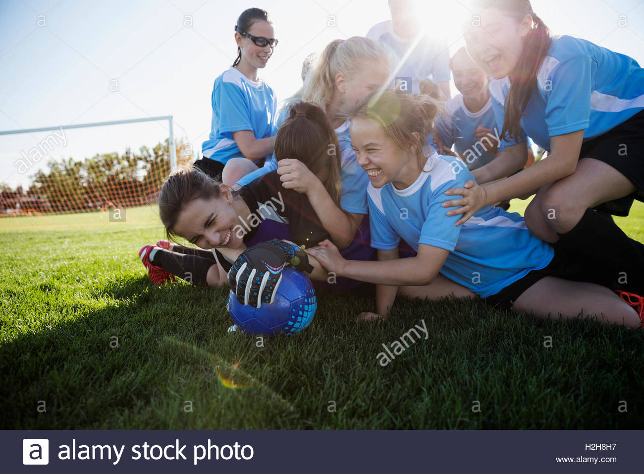 Playful middle school girl soccer team celebrating in pile on sunny