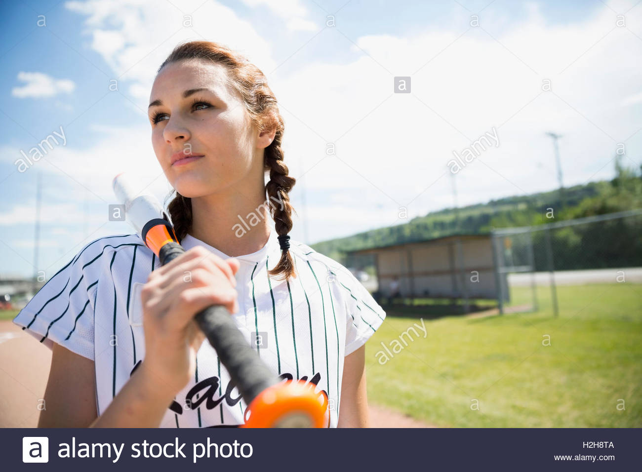 Serious middle school girl softball player holding bat on sunny field