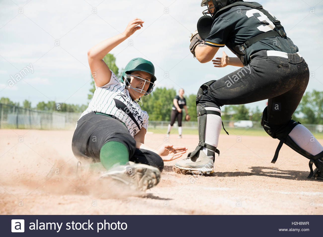 Middle school girl softball player sliding into home base next to