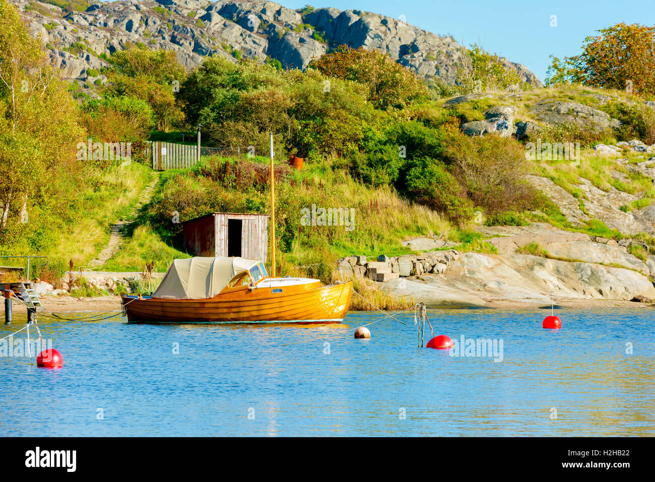 Old wooden motorboat with sailing mast moored in seaside bay close to cliffs and shrubbery. Stock Photo