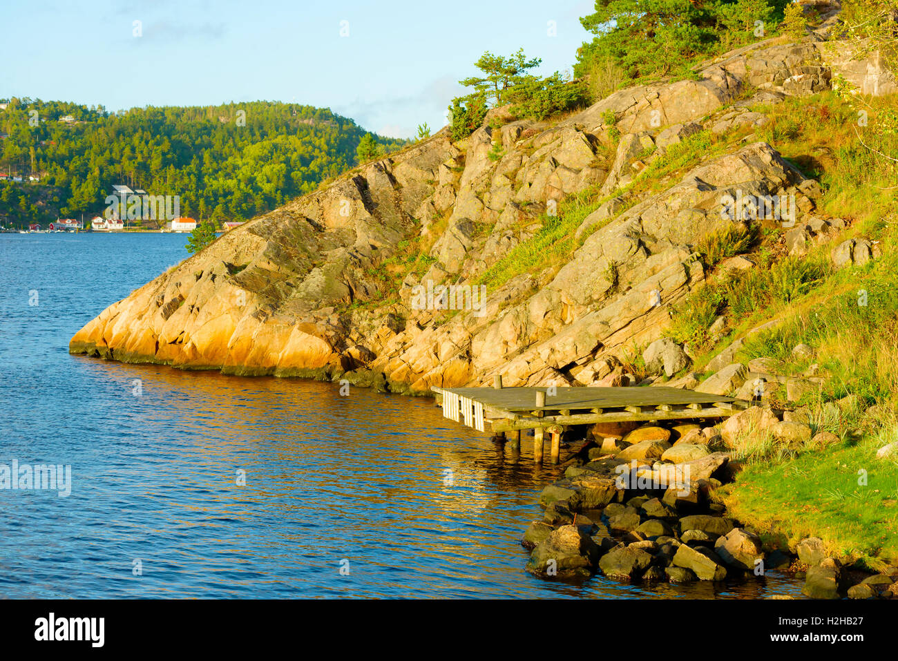 Evening sunshine on wooden pier on rocky shore. Saltbacken in Sweden, close to Norway (the houses and forest in the background). Stock Photo