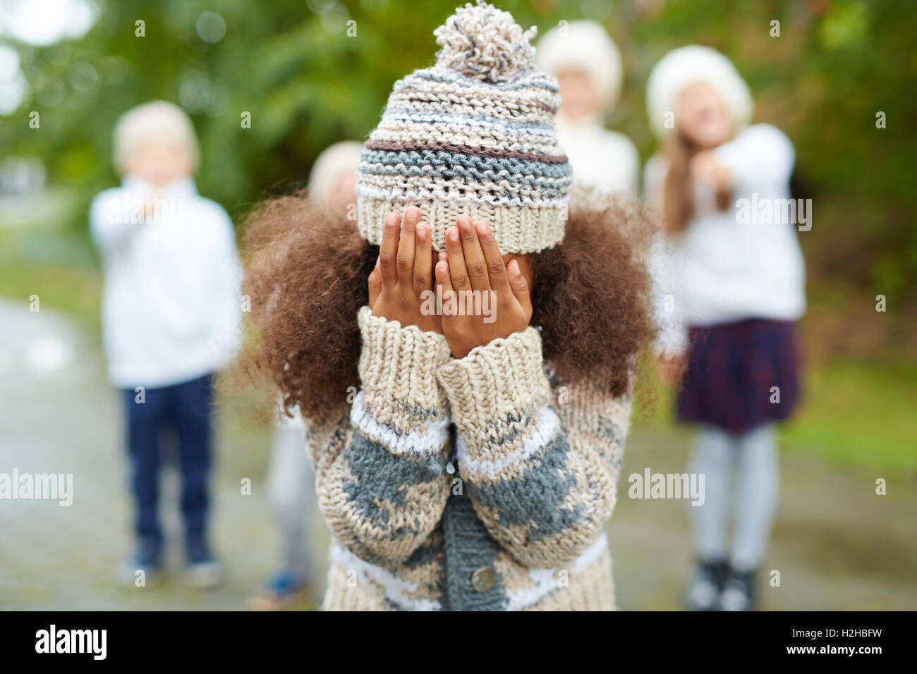 Crying girl hiding her face while classmates mocking at her Stock Photo