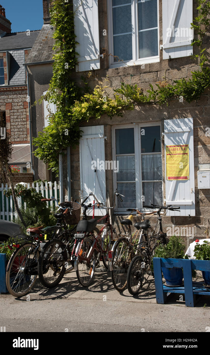 The coastal commune of Barfleur in Normandy northwest France. Tourist cycles parked outside a granite house with shutters Stock Photo