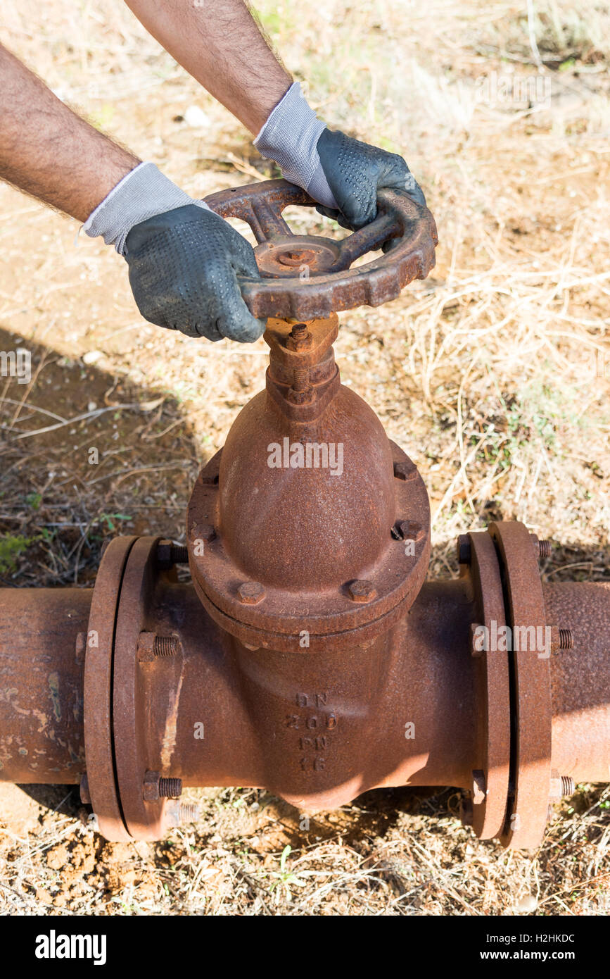 Hands with Work Gloves Clutching a Pipe Valve of a very old and Rusty Water line Stock Photo