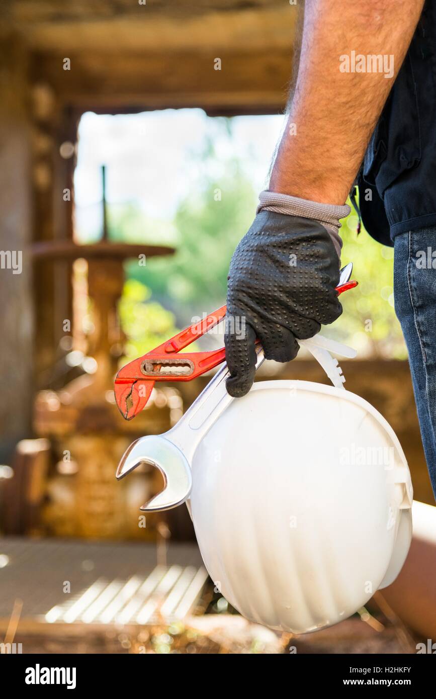 Hands with work gloves holding a safety helmet, a wrench and a red key pipe clamps Stock Photo