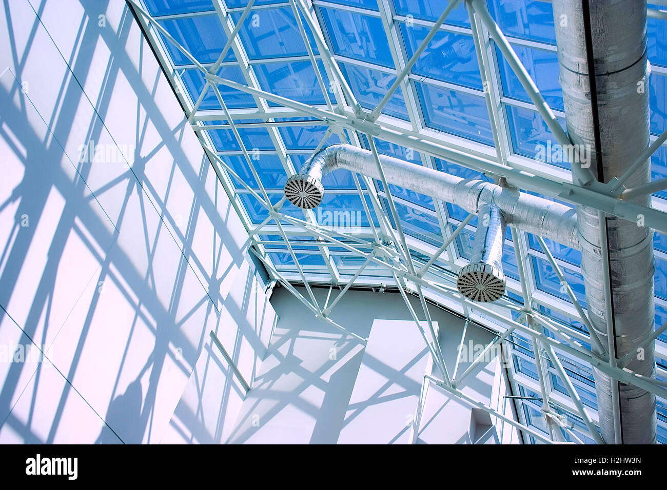 Glassy roof of contemporary business style  building with ventilation tubing, blue sky, sunlight and shadows and light playing. Stock Photo