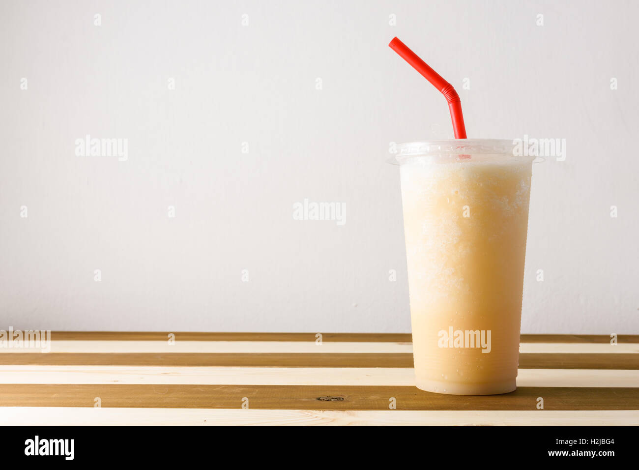 smoothies of fruit juice in plastic glass on wooden background with red tube Stock Photo