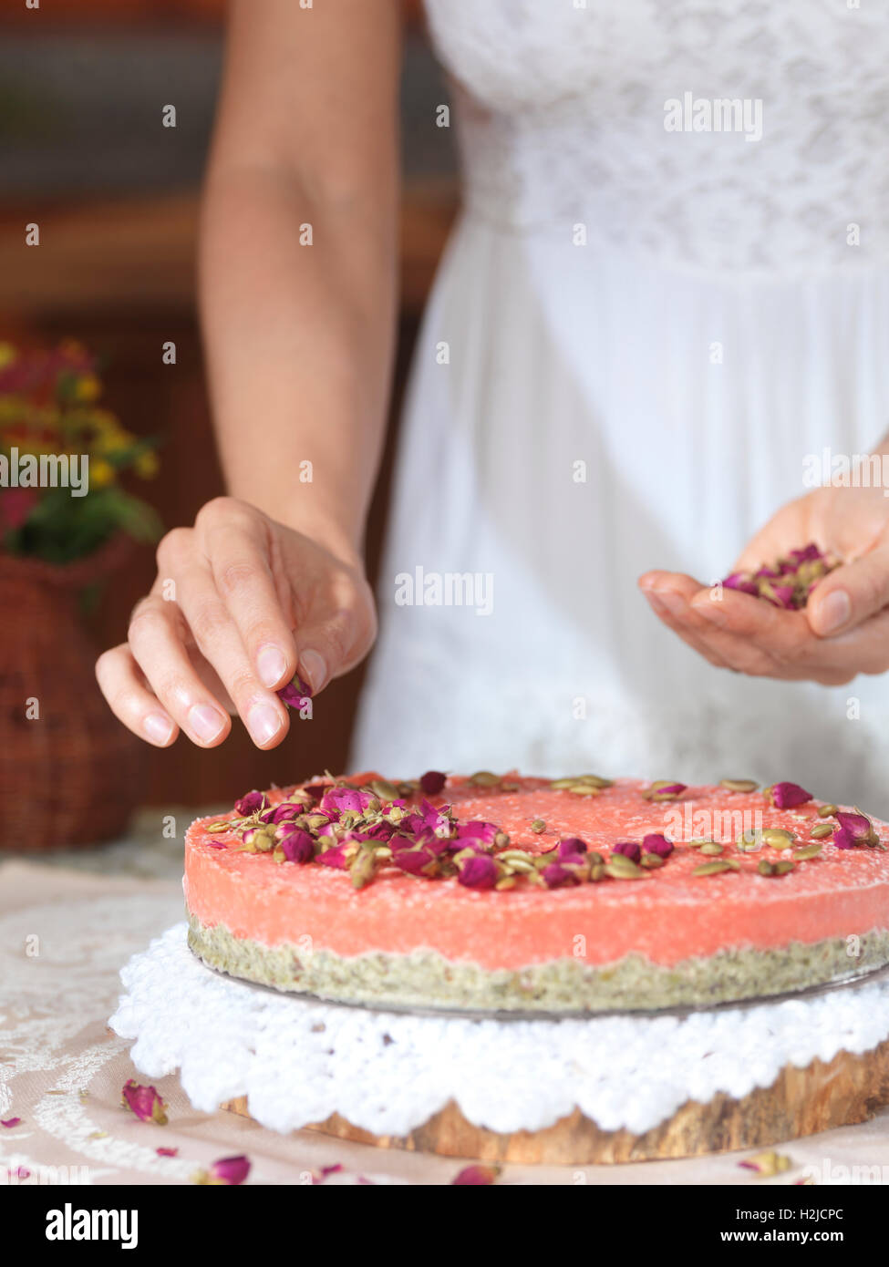 Closeup of woman hands decorating a home-made fruit cake with rose buds at home Stock Photo