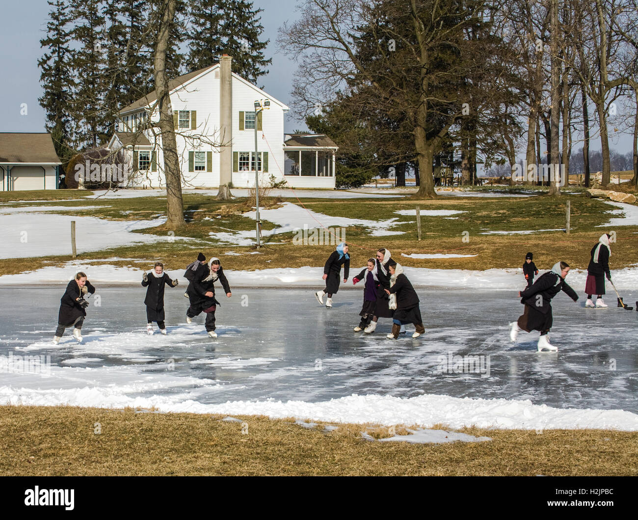 Amish children ice skating on a pond and a white farmhouse, Lancaster