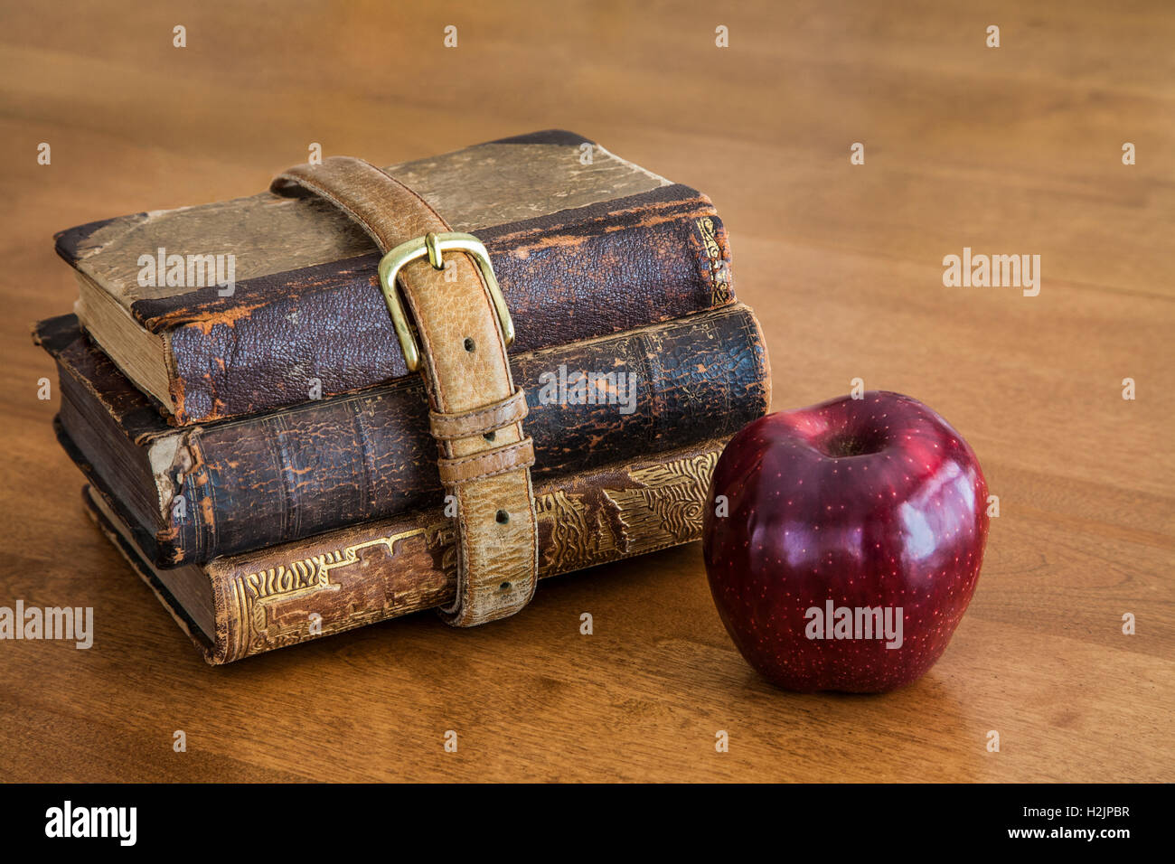 Three old school books wrapped with an old belt with one red apple for the teacher abstract on wood, USA, vintage objects still life, antique images Stock Photo
