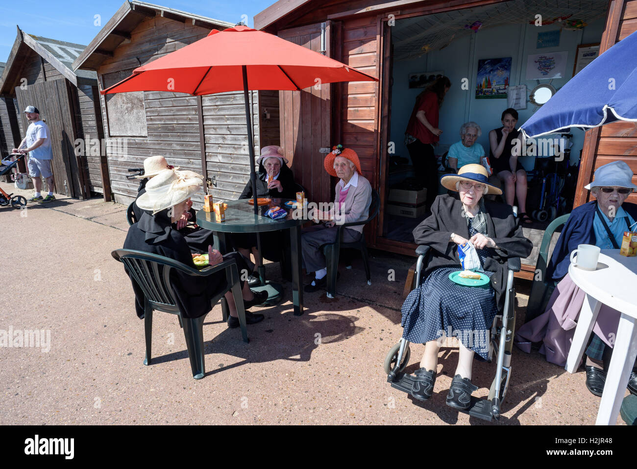 Group of elderly people sitting outside a wooden painted beach hut drinking orange juice during the summer of 2016 Stock Photo