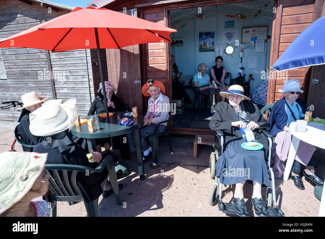 Group of elderly people sitting outside a wooden painted beach hut drinking orange juice during the summer of 2016 Stock Photo