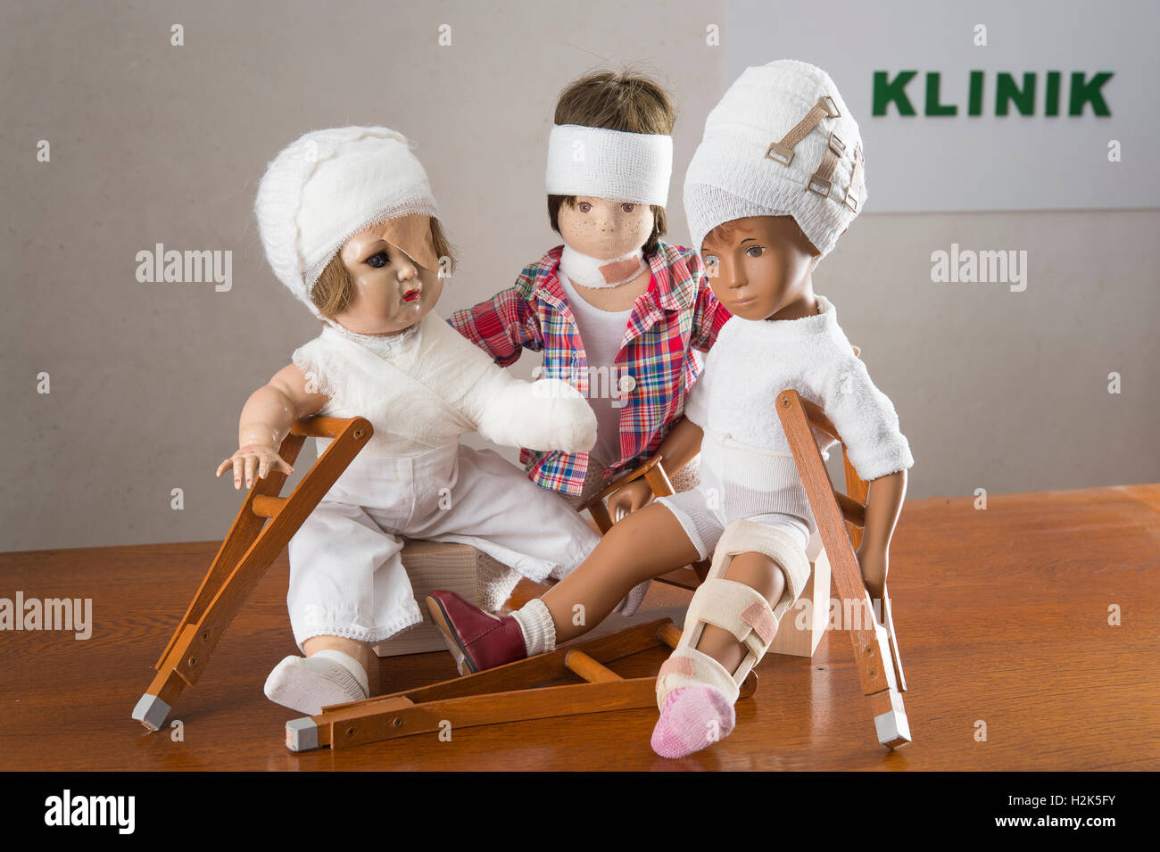 Three dolls sitting, bandages on head, leg splint, crutches, eye patches, Armverband, shoulder bandage and frill Stock Photo