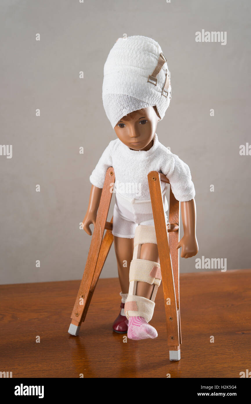 Doll with bandaged head, leg splint, crutches, walking upright, frontal view Stock Photo