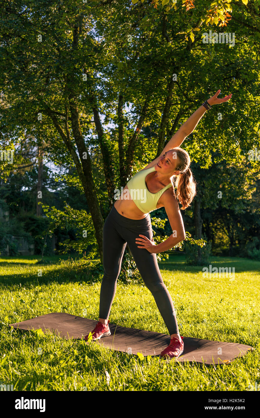 Warmup exercise, young woman in sportswear doing workout on mat in park, Munich, Upper Bavaria, Bavaria, Germany Stock Photo