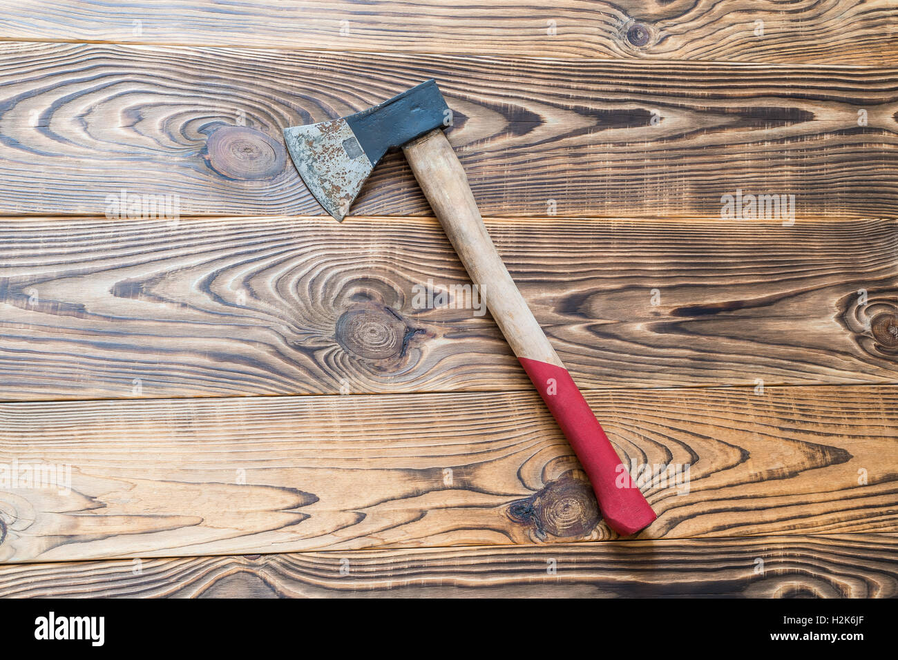 Big rusty ax with long red handle on aged natural wooden background Stock Photo