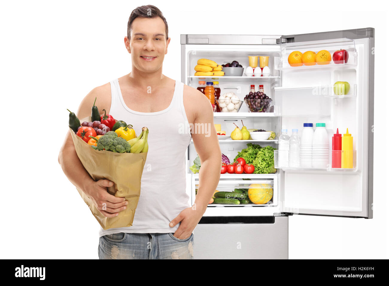 Man posing with a shopping bag full of groceries in front of an open fridge isolated on white background Stock Photo