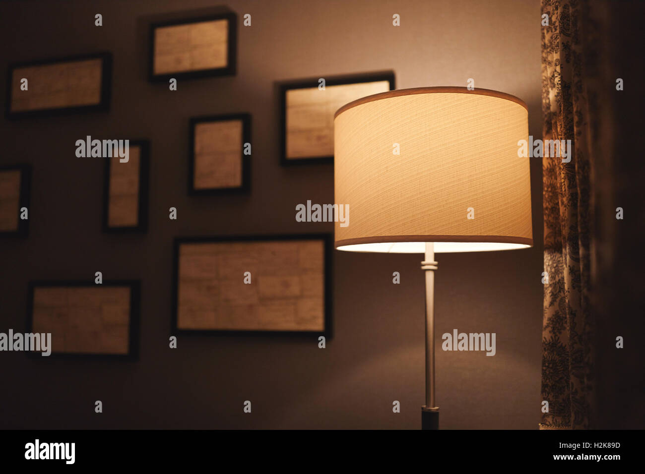 A lamp in a dark corner of a hotel room with abstract frames out of focus on the wall behind it and a curtain to the right. Stock Photo