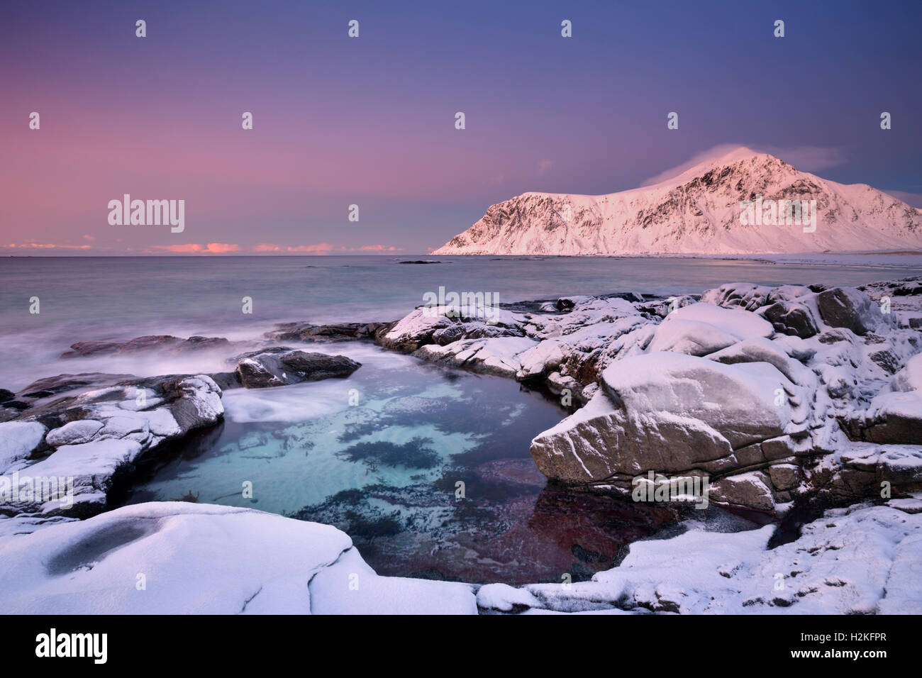 Alpenglow at the rocky beach of Skagsanden on the Lofoten in northern Norway, photographed at dusk in winter. Stock Photo