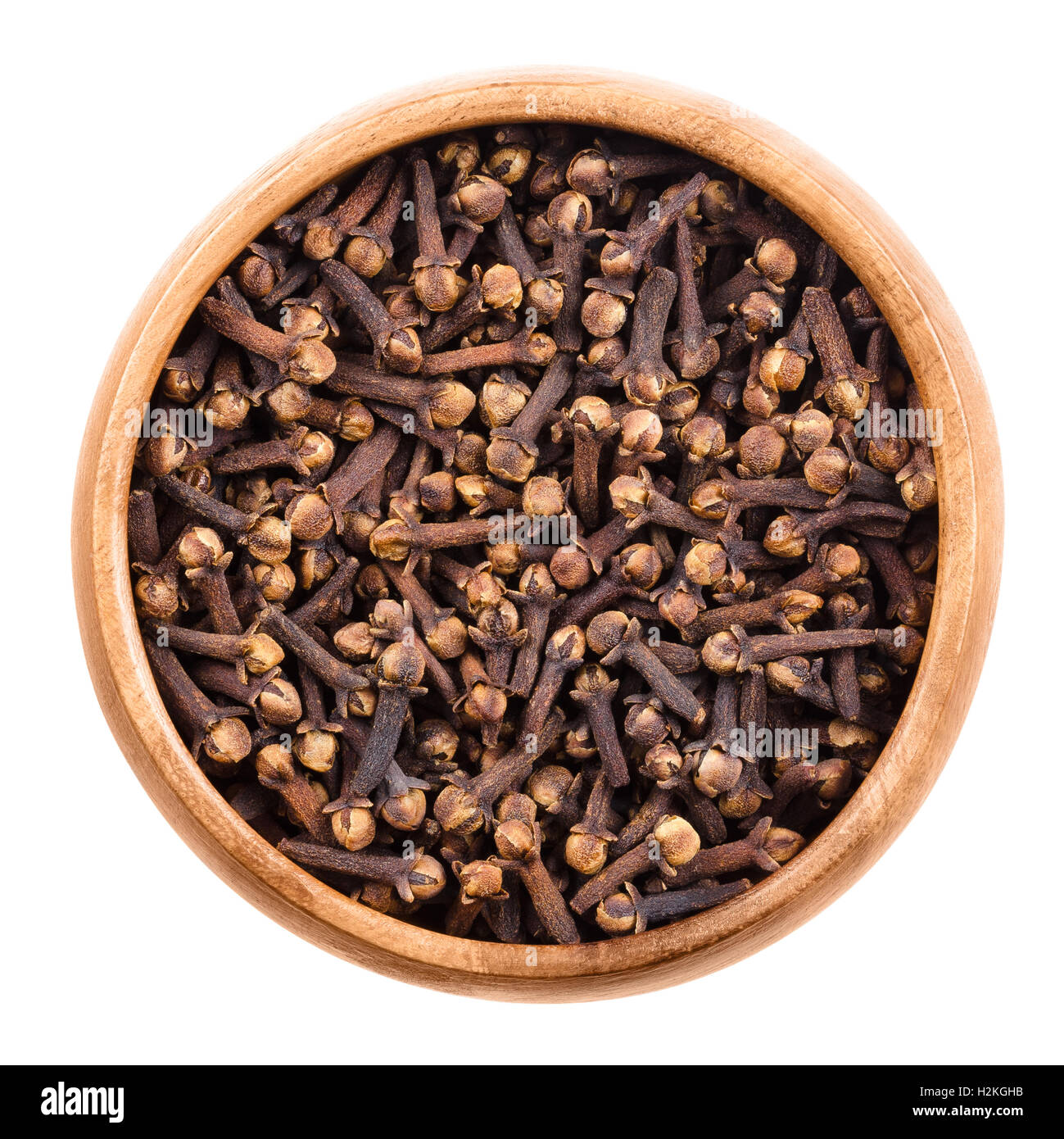 Dried cloves in a wooden bowl on white background. Brown aromatic flower buds of Syzygium aromaticum, commonly used as spice. Stock Photo