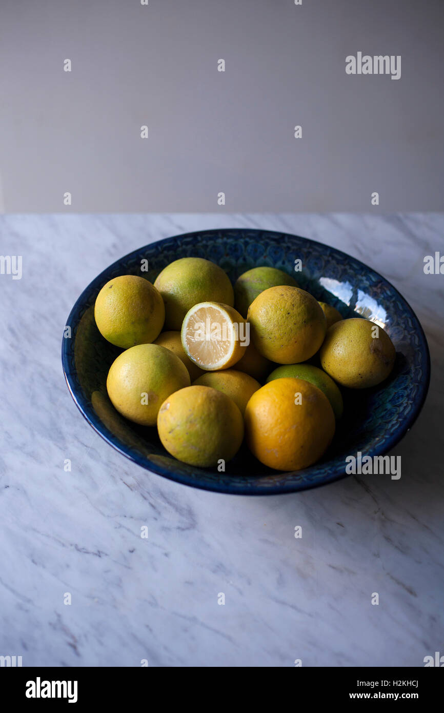 Fresh organic lemons in a blue bowl on white marble table Stock Photo
